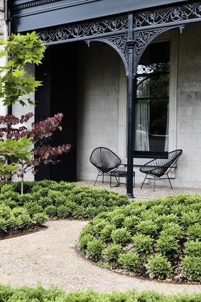 A Jencks-style formal garden with cloud-pruned plantings adjoins a tiled front patio, which has been restored with original tessellated tiles sourced from England.