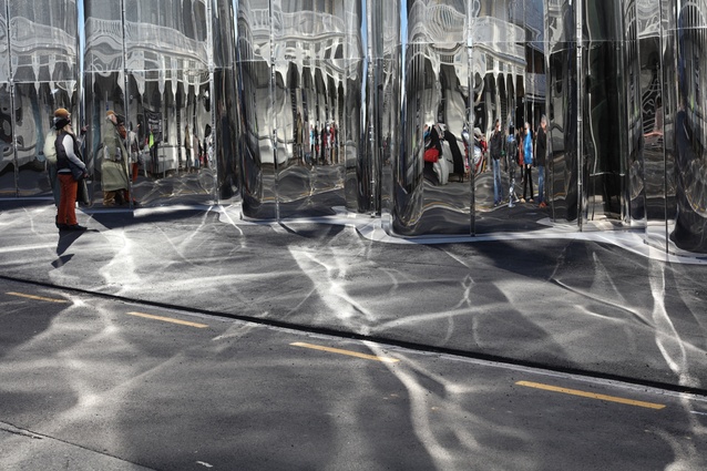 The facade's highly reflective surface creates moving shadows over the street.
