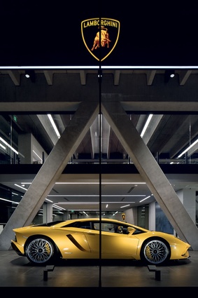 The Lamborghini Aventador is framed by the angled concrete beam structure in the front windows.
