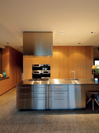 In the open-plan kitchen, the clean lines of the polished metal island and rangehood complement the light, contemporary look of the interior. 