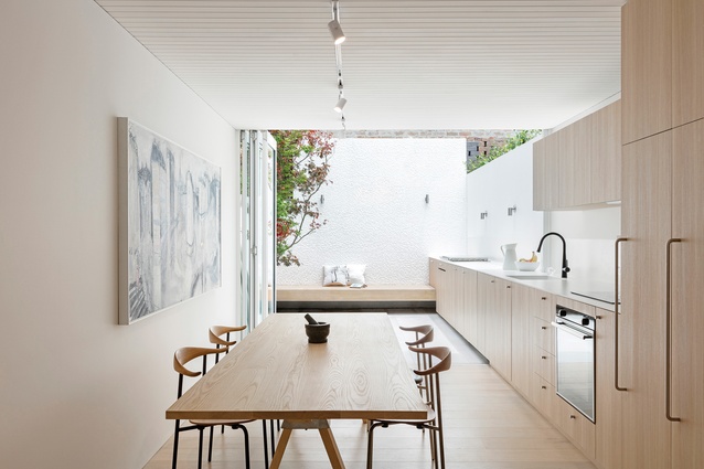 The kitchen extends seamlessly through bifold doors to a sunlit courtyard. Artwork: Mark Hanman.