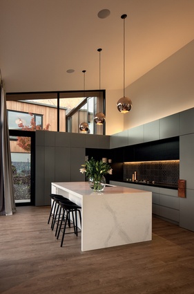 The kitchen has a high ceiling stud, and features copper pendants and large windows on two sides. 
