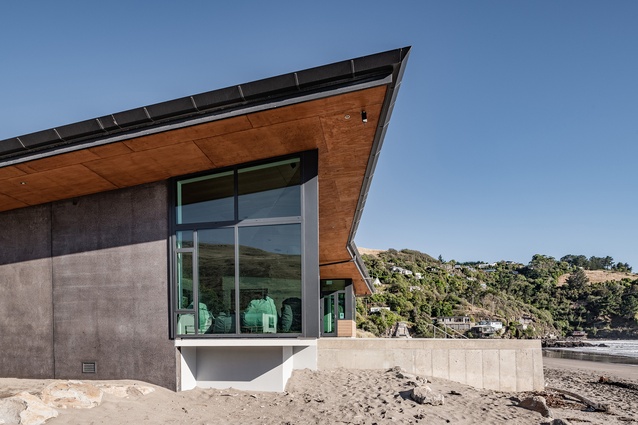 The angular black roofline references the rocky outcrops at either end of the beach.