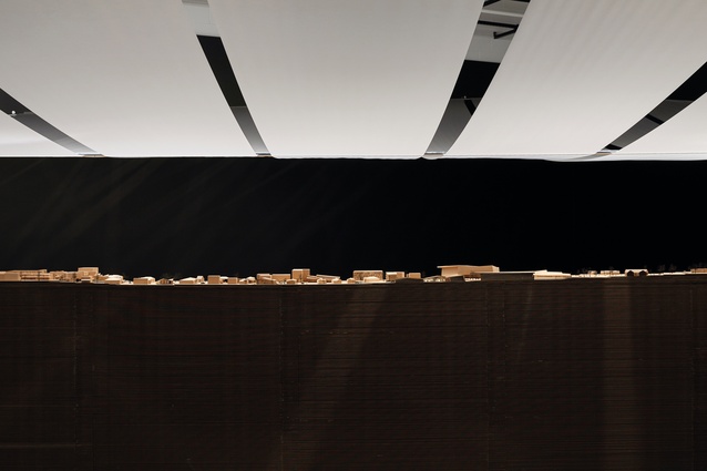 The models sit on a diagonal plinth of stacked corrugated cardboard, with ribbons of white tracing paper overhead.