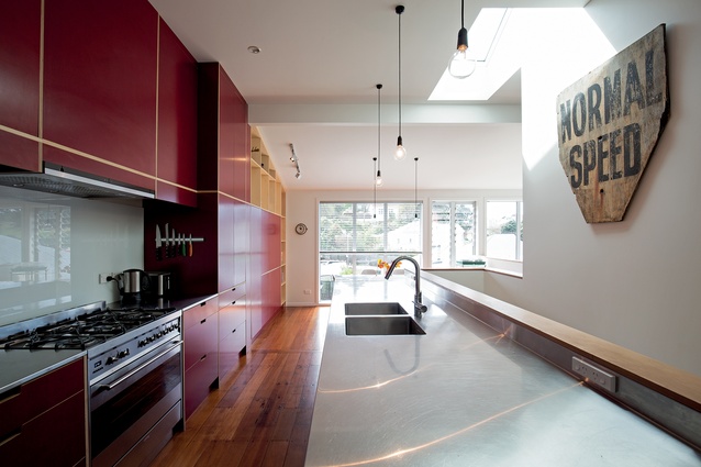 The striking red galley-style kitchen has a staircase behind the bench, with built-in shelving. This enables an open-plan, light-filled living and dining area with views onto the garden.