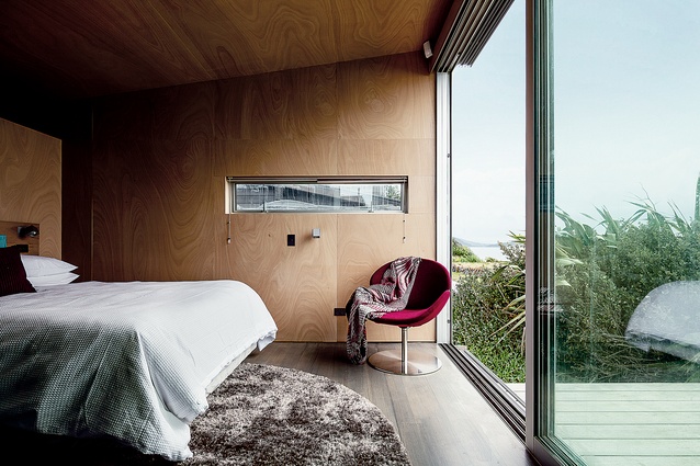 <a href="http://architecturenow.co.nz/articles/to-the-island/" target="_blank"><u>Kapiti House</u></a>. The master bedroom has views of Kapiti Island and a red BoConcept armchair.