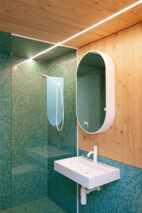 The guest bathroom is tiled in a rich sea-green and accented with warm cypress wood and bright-white hardware.