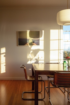There is a play of light and shadows in the dining room where a photograph (<em>Boatman</em> by Stuart Broughton) hangs near a Milo Baughman Parsons-style dining table in burl wood. The couple added Marcel Breuer chairs – all are from Mid Century Swag. The pendant is Cloud from Vitrine.