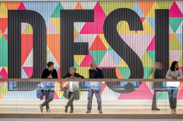 Visitors stand in front of a colourful permanent exhibition.  
