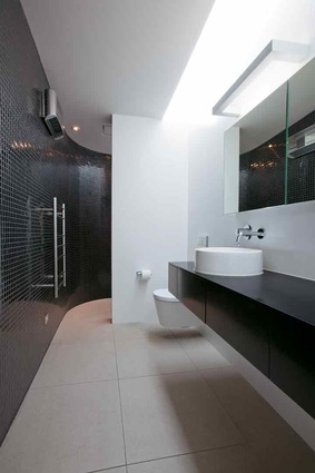 The glossy black tiles in the bathroom curve at one end into the shower area.