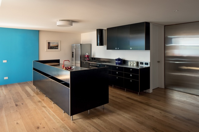 The kitchen is bold with its free-standing black cabinetry and blue-painted feature wall.