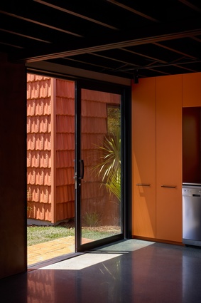 Melteca melamine-finished kitchen cabinetry – green in one house, orange in the other – introduce personality to the dwellings.