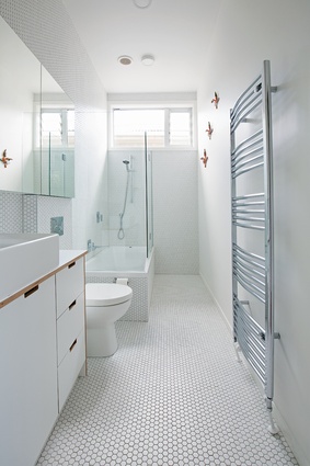 The all-white bathroom features hexagonally tiled flooring and a bespoke ply-edged vanity. 