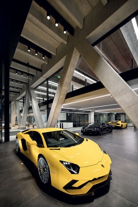 The Lamborghini Aventador is framed by the angled concrete beam structure in the front windows.