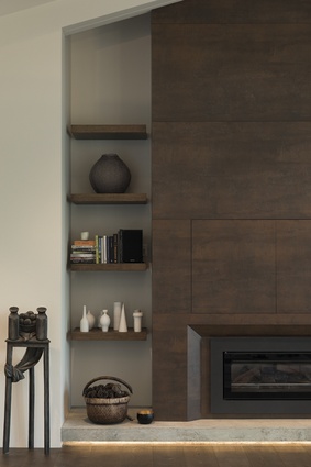 The fireplace is clad in Neolith ceramic tiles in Iron Corten, which gives a rustic aesthetic to the space. Floating shelves provide storage on either side of the chimney, which also conceals a TV.