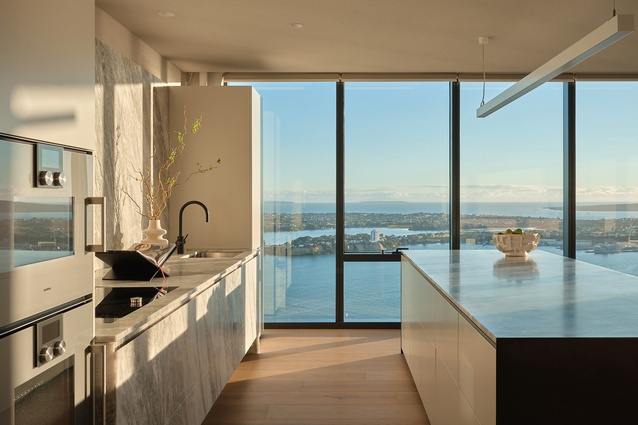 Floating kitchens with recessed lighting and timber grain interplay 178 metres above Britomart — interiors developed through trans-Tasman collaboration within Plus Studio.