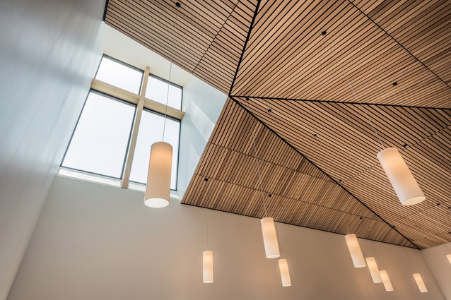 A high-level timber-panelled ceiling has a dynamic geometry that draws the eye upwards towards a light-well spire. It also acts like an acoustic damper.