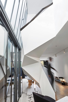 A faceted steel stair spirals up through a void at the centre of the open-plan living area.