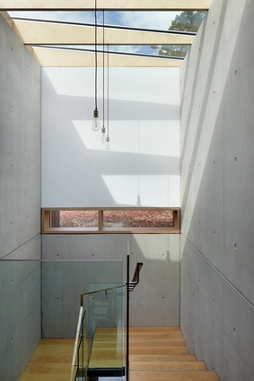 The main staircase features a skylight and double-height exposed concrete walls, making for a dramatic vertical transition from ground floor to upper level.