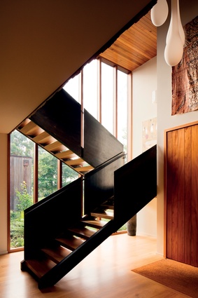 At the entry, a sculptural staircase of steel and timber zig-zags across a double-height window with a garden view beyond.