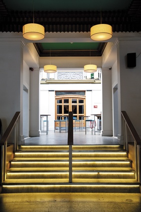 The bright illumination of the light well is visible  from the main circulation axis. Low-ceilinged nooks sit opposite each other just above the stairs, which were imbued with gold, art deco-referencing lighting.
