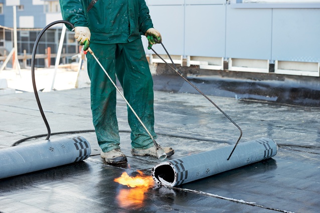 A roofer installs torch-on roof membrane.