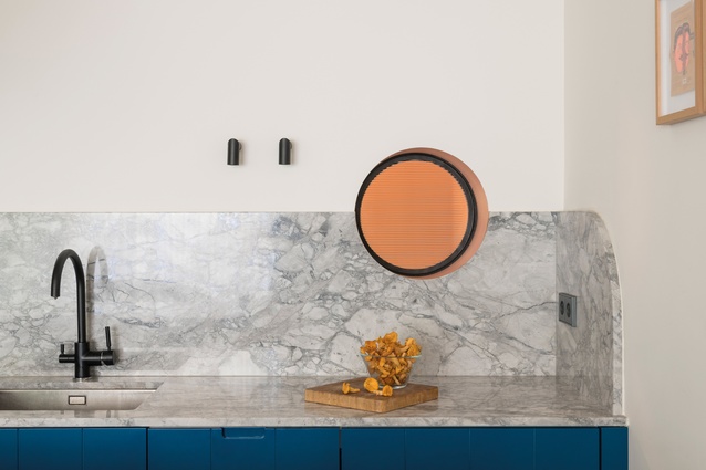 Glowing and salmon-coloured, a fluted glass window hints at the bathroom behind the kitchen.