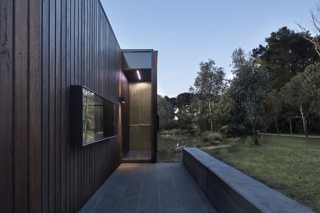 Visually anchored by a rammed-earth wall, the timber-clad retreat stretches beyond the bank of the pond.