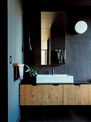 The bathroom boasts a dark, sophisticated palette, offset by the warmth of solid American oak joinery.