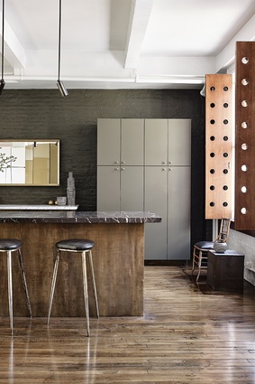 The earth-toned kitchen features vintage bar stools and a brass-clad, marble-topped island.