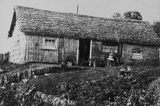 View of a mother and infant sitting outside a raupō house in Taranaki, photographed 1875–1885, by William Andrews Collis of New Plymouth. A baby’s phaeton may be seen in the doorway.