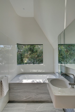 An inviting bathtub sits under a curved window, allowing the bather to feel as if they are among the trees.