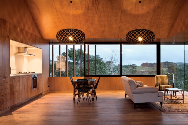 The kitchen, dining and living area is lined in plywood with horizontal windows offering a view over Onetangi Beach.
