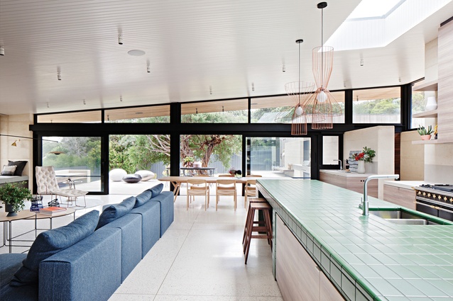A green-tiled bench references foliage and defines the kitchen within the open-plan space.