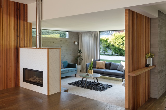A <a 
href="https://thefireplace.co.nz/gazco_studio_duplex_gas_fire.html"style="color:#3386FF"target="_blank"><u>Gazco Studio</u></a> duplex gas fire acts as a divider between the kitchen and living spaces, while also efficiently heating both rooms and the entire house. The herringbone tiles surrounding the fireplace are framed in cedar.
