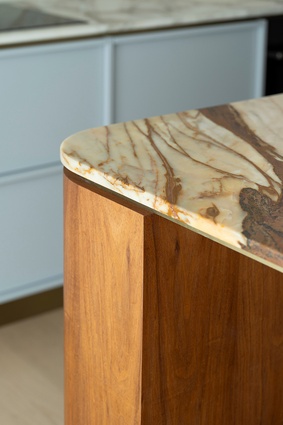 The kitchen island is topped with an ochre, umber and beige-coloured quartz bench, wrapped in warm oak surrounds and finished with brass detailing. 